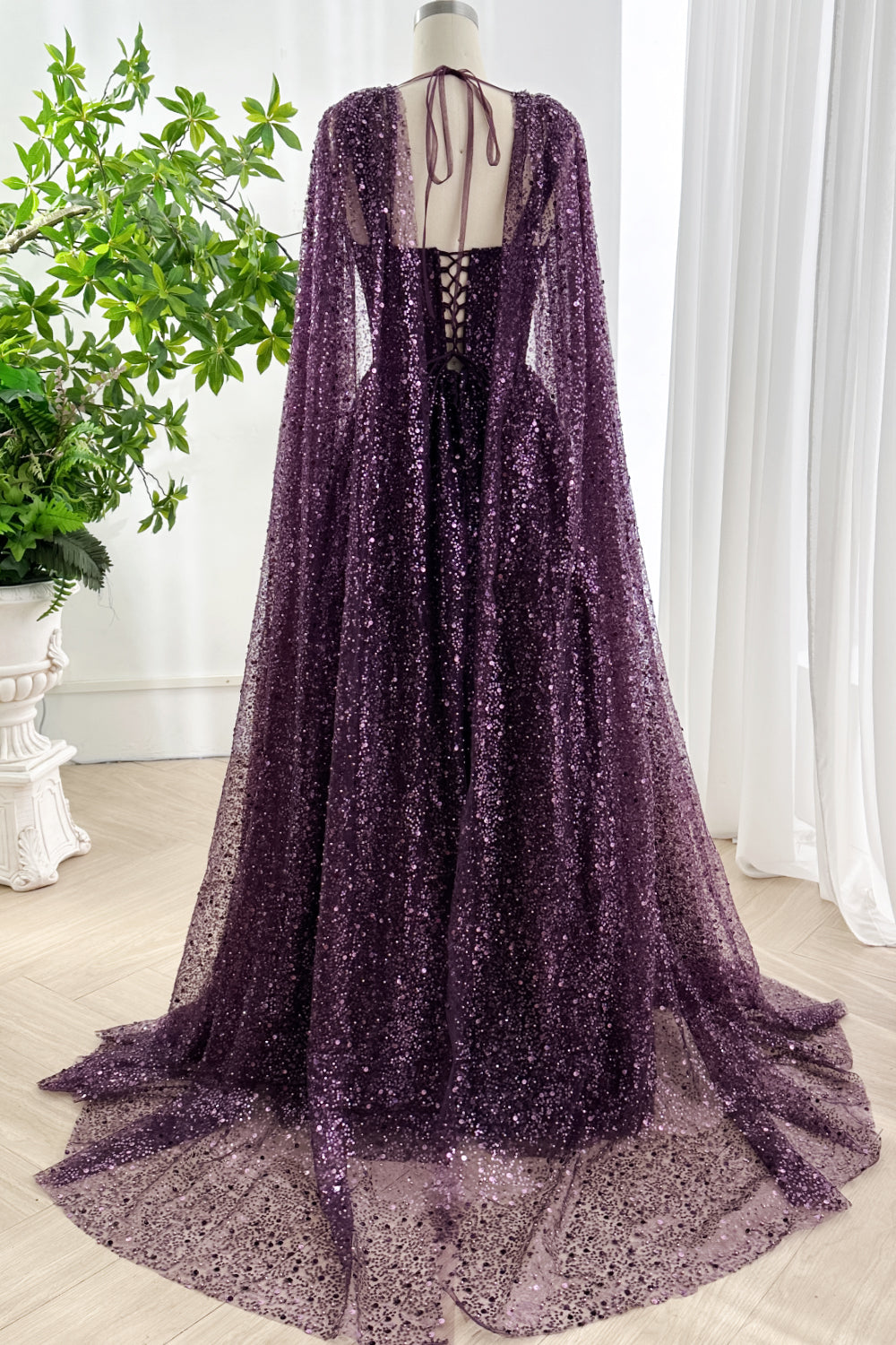 Rear full view of dark violet sparkling gala gown with long sequin cape and soft train beautifully displayed in minimalist studio setup