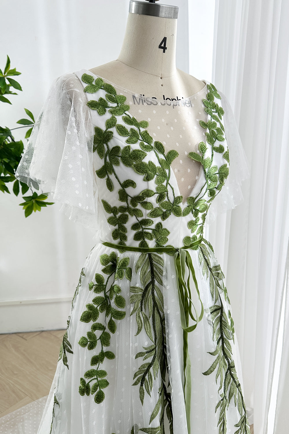 Close-up of embroidered bodice with green leaf appliqué and tied ribbon waist on soft tulle gown