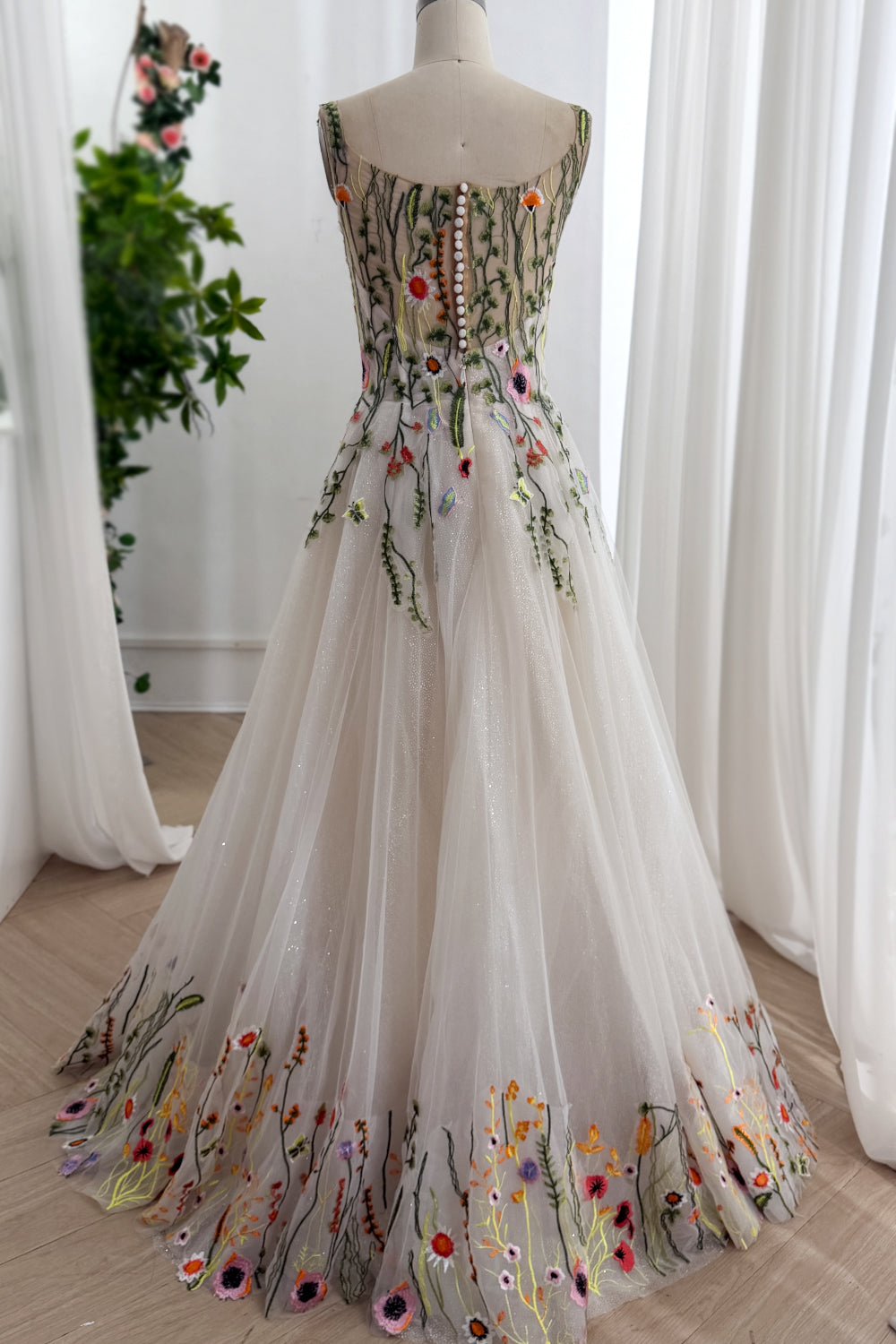 Reverse angle highlights buttoned closure shimmer skirt bud border trailing hem graceful outdoor aisle attire showroom scene.