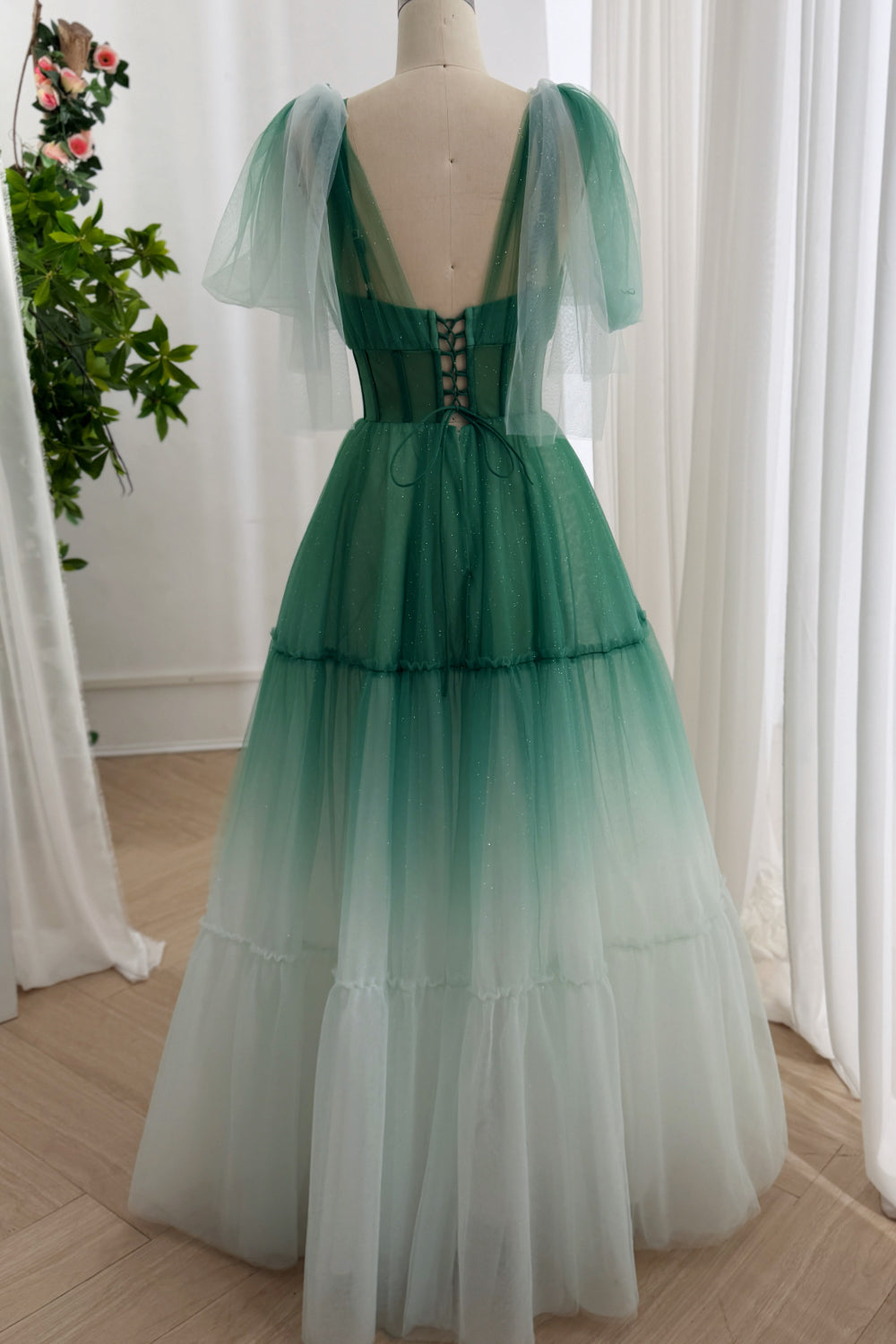 Rear view seafoam layered A-line attire featuring boned lacing, floor hem, gathered tiers, dreamy garden backdrop, editorial.