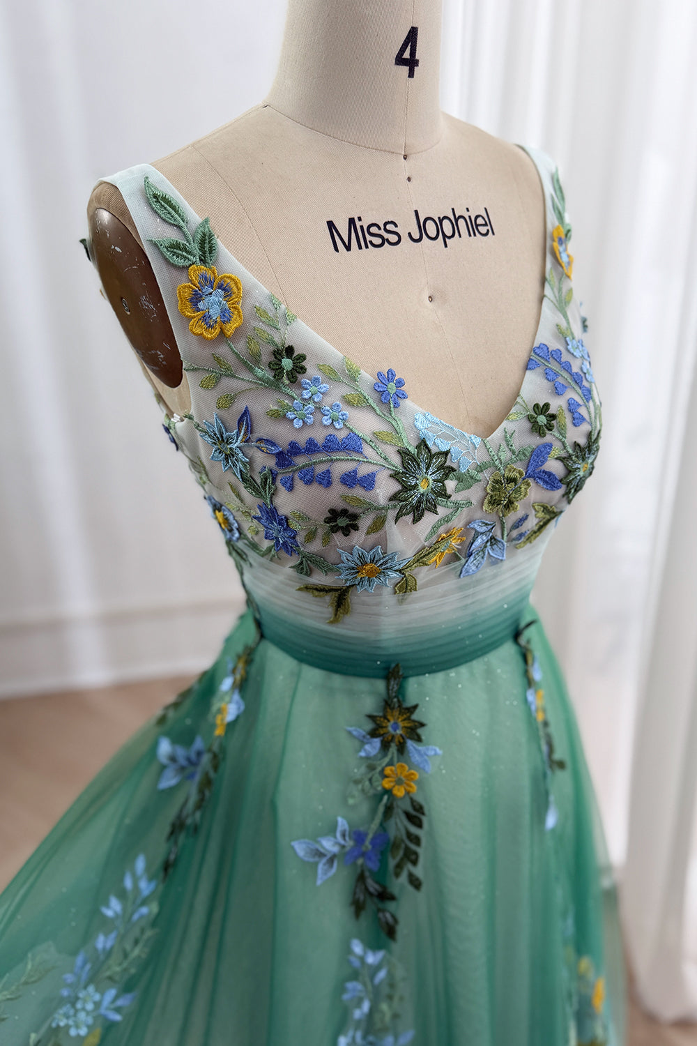 Macro crop reveals white-teal fade, colorful wildflowers, sleeveless illusion overlay, fairytale prom ensemble detail imagery
