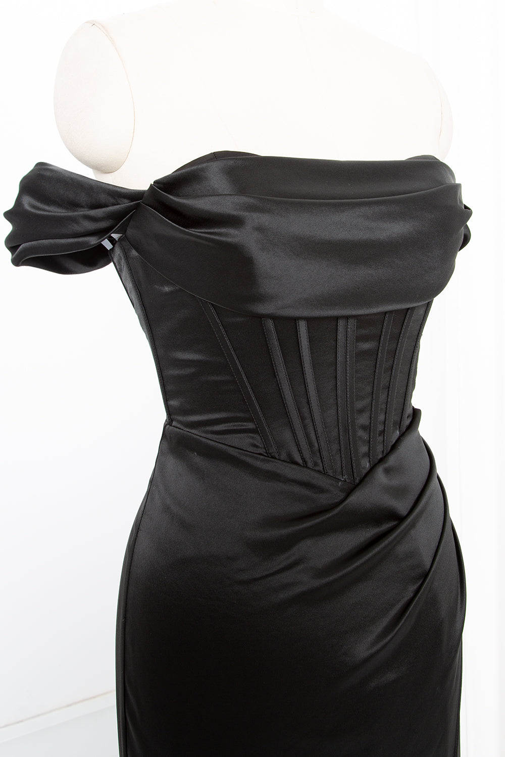 Luxury black satin gown close-up highlighting draped off-shoulder neckline and structured corset bodice detailing for upscale occasions