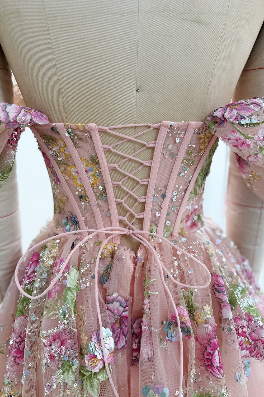 Close-up of pink crisscross corset lacing tied in a bow on the back of a floral embroidered and sequined blush pink dress.