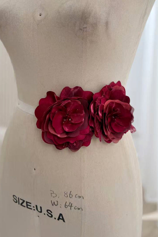 Two dimensional burgundy fabric rose flowers displayed side by side at the waist of a dress form.