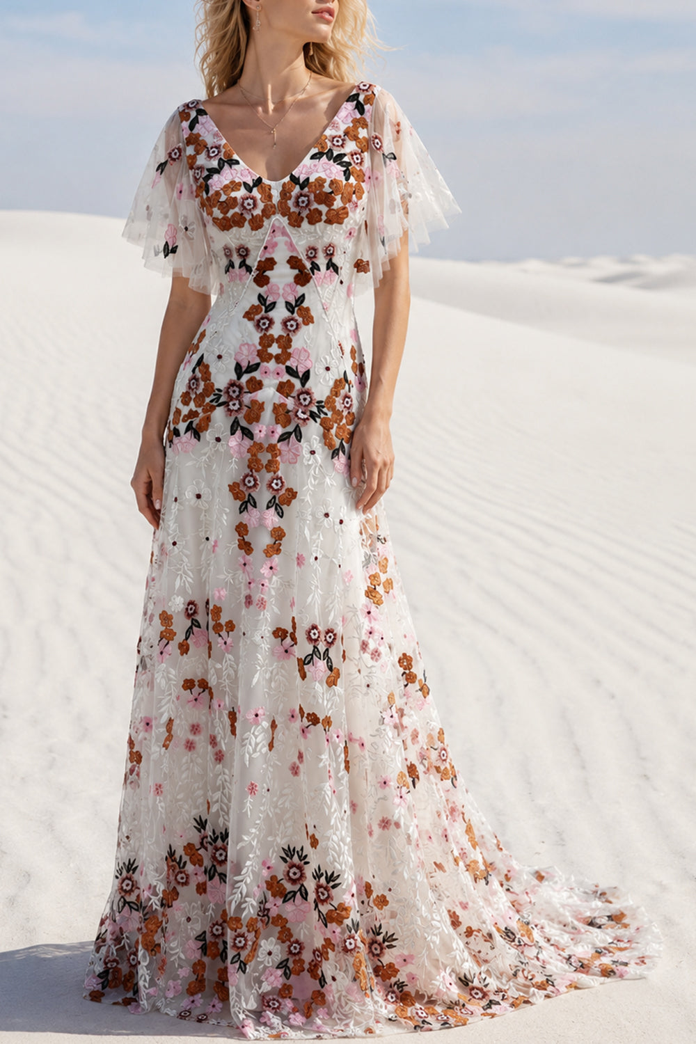Model wearing an ivory multicolor floral embroidered floor-length gown in a white desert setting