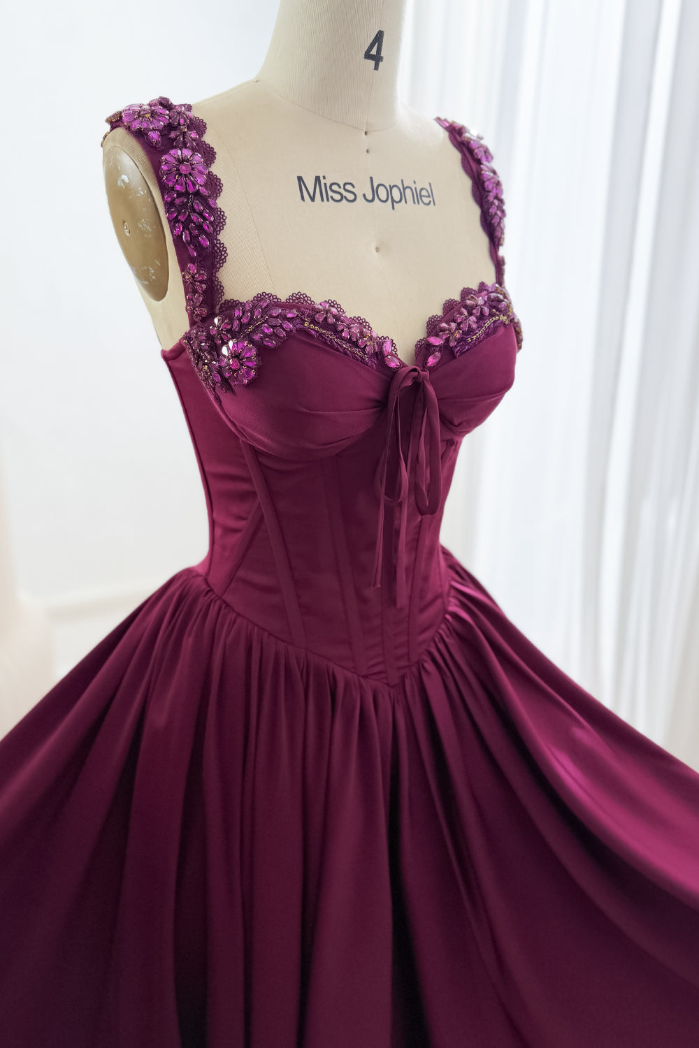 Angled bodice detail of plum dress showing sparkling floral trim, scalloped lace, sweetheart neckline, and corset seams.
