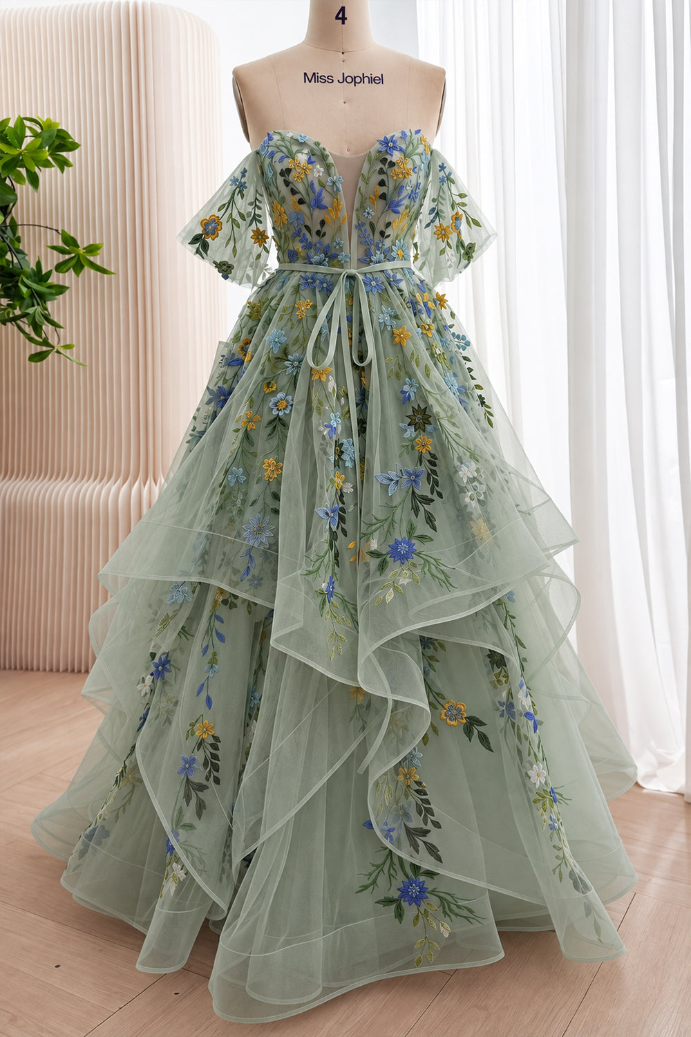 Front view of a sage green wildflower embroidered tulle gown with off-the-shoulder flutter sleeves and a full cascading ruffle skirt.