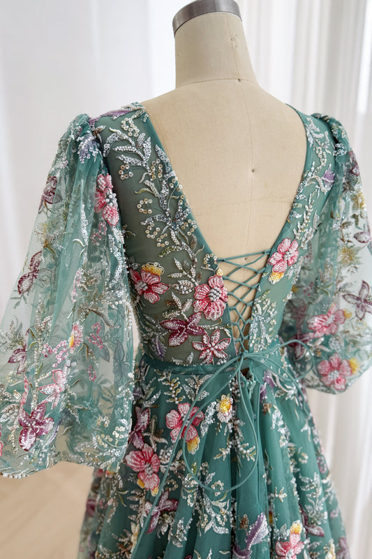 Close-up back view of the teal floral embroidered gown showing its low V-back, lace-up closure, and sheer flared sleeves
