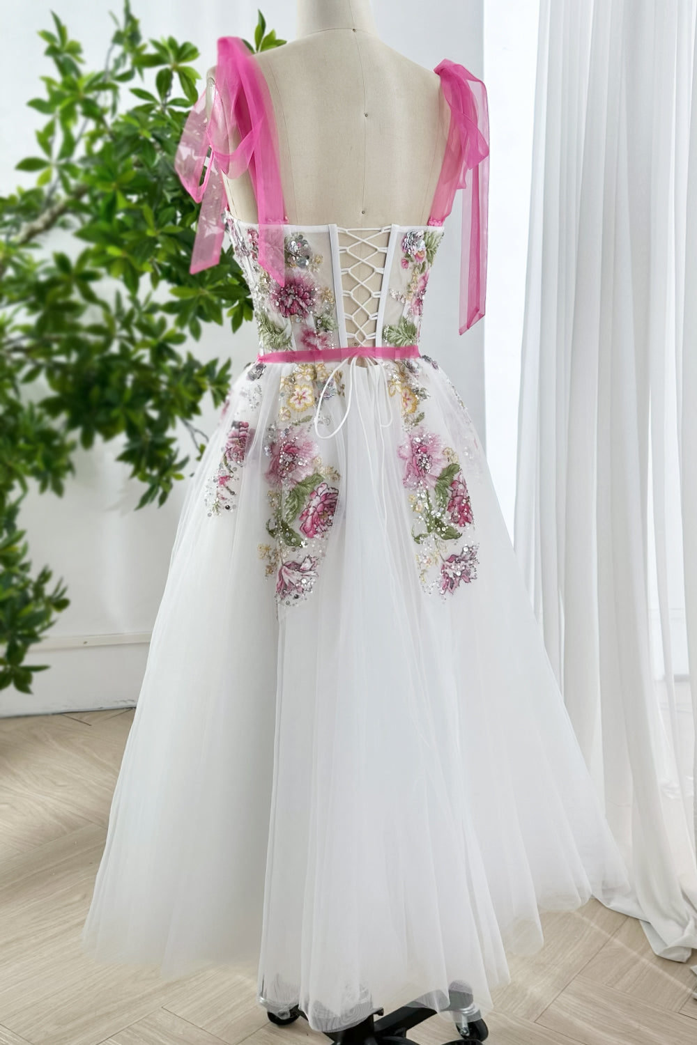 Elegant embroidered tulle gown with corset lace up back, pink ribbons, and sequin floral appliqué styled on mannequin rear view