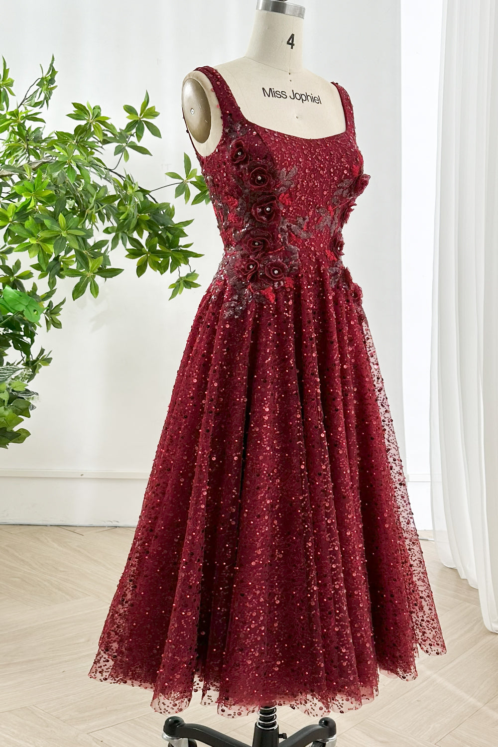 Three-quarter perspective highlights A-line sweep, sparkling overlay, graceful movement, cocktail sophistication, gallery greenery ambience scene