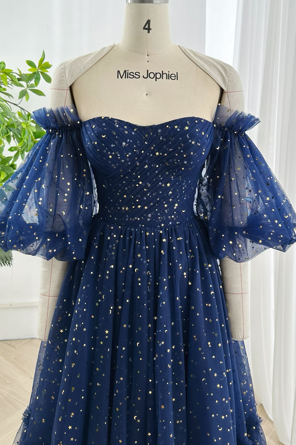 Galaxy inspired navy mesh dress with shimmering gold star pattern sweetheart bodice and off-shoulder design elegantly shown on mannequin in daylight