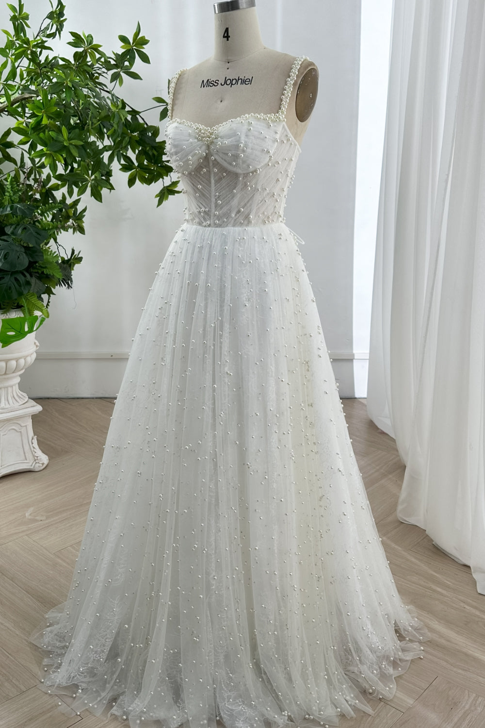 Elegant floor-length A-line tulle bridal gown covered in pearl embellishments displayed in bright natural light studio setting