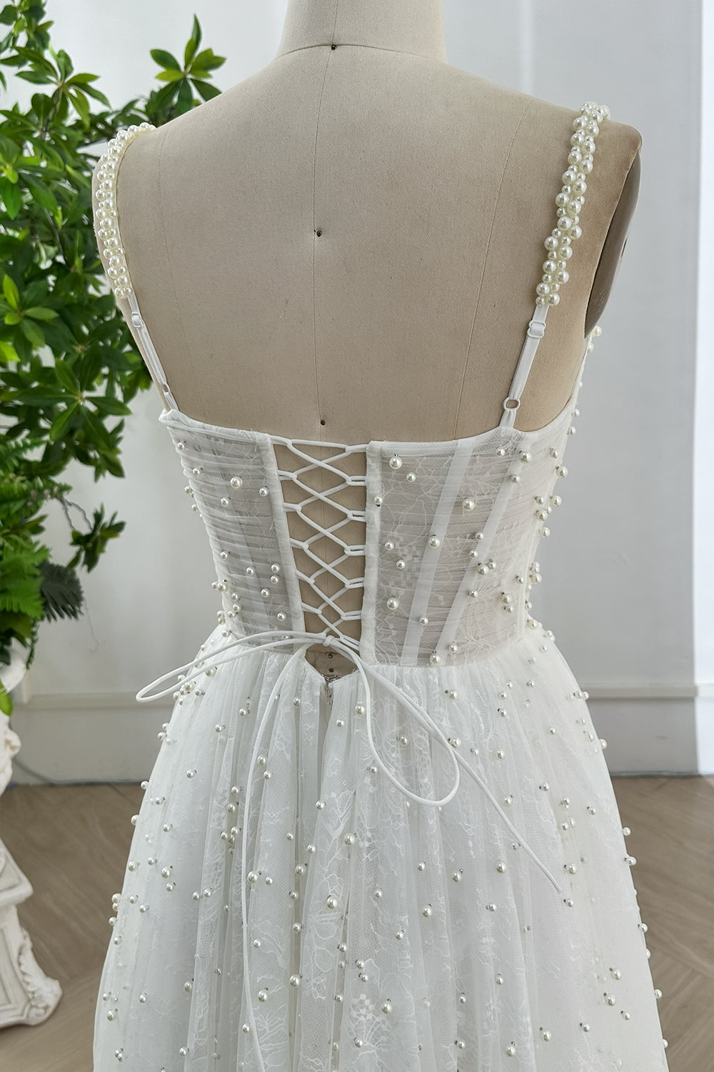 Close-up of lace-up back and pearl-beaded straps on ivory tulle bridal gown highlighting fine handcrafted pearl detail