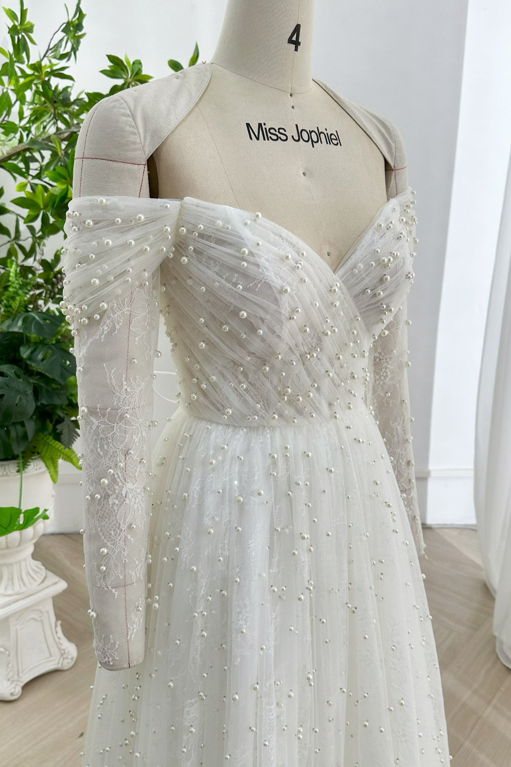 Soft white beaded lace bridal dress showing fitted bodice off shoulder sleeves handmade pearl accents ideal for romantic indoor celebration