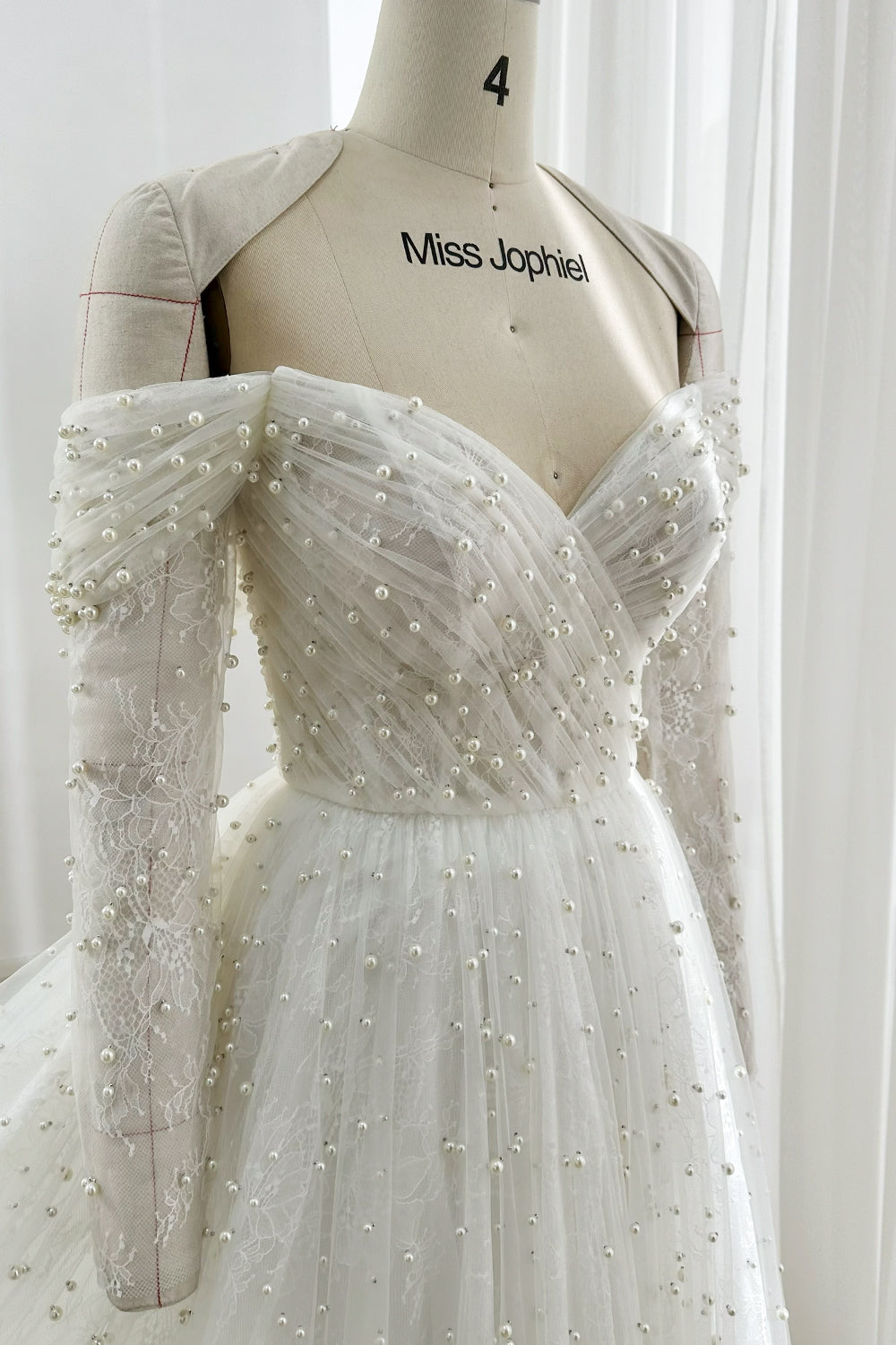 Graceful ivory lace wedding dress with off-shoulder sweetheart neckline and pearl detailing for modern romantic brides indoor ceremonies