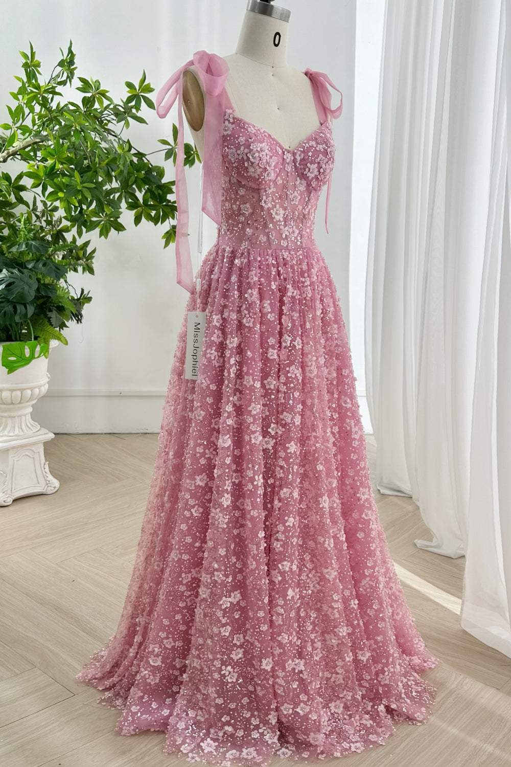 Delicate floral embroidered tulle gown featuring corset bodice and ribbon shoulder straps set against white draped curtain background