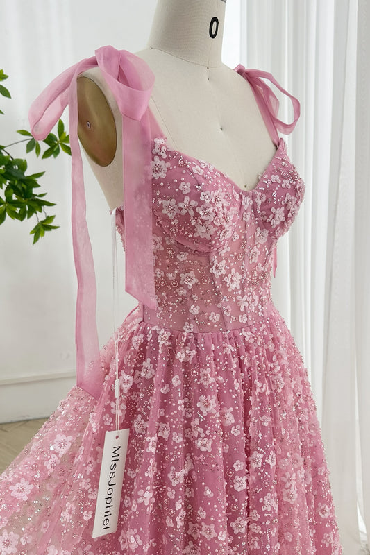 Romantic pink floral tulle corset gown with sheer bodice, sequin detailing, and soft ribbon shoulder bows displayed on mannequin indoors