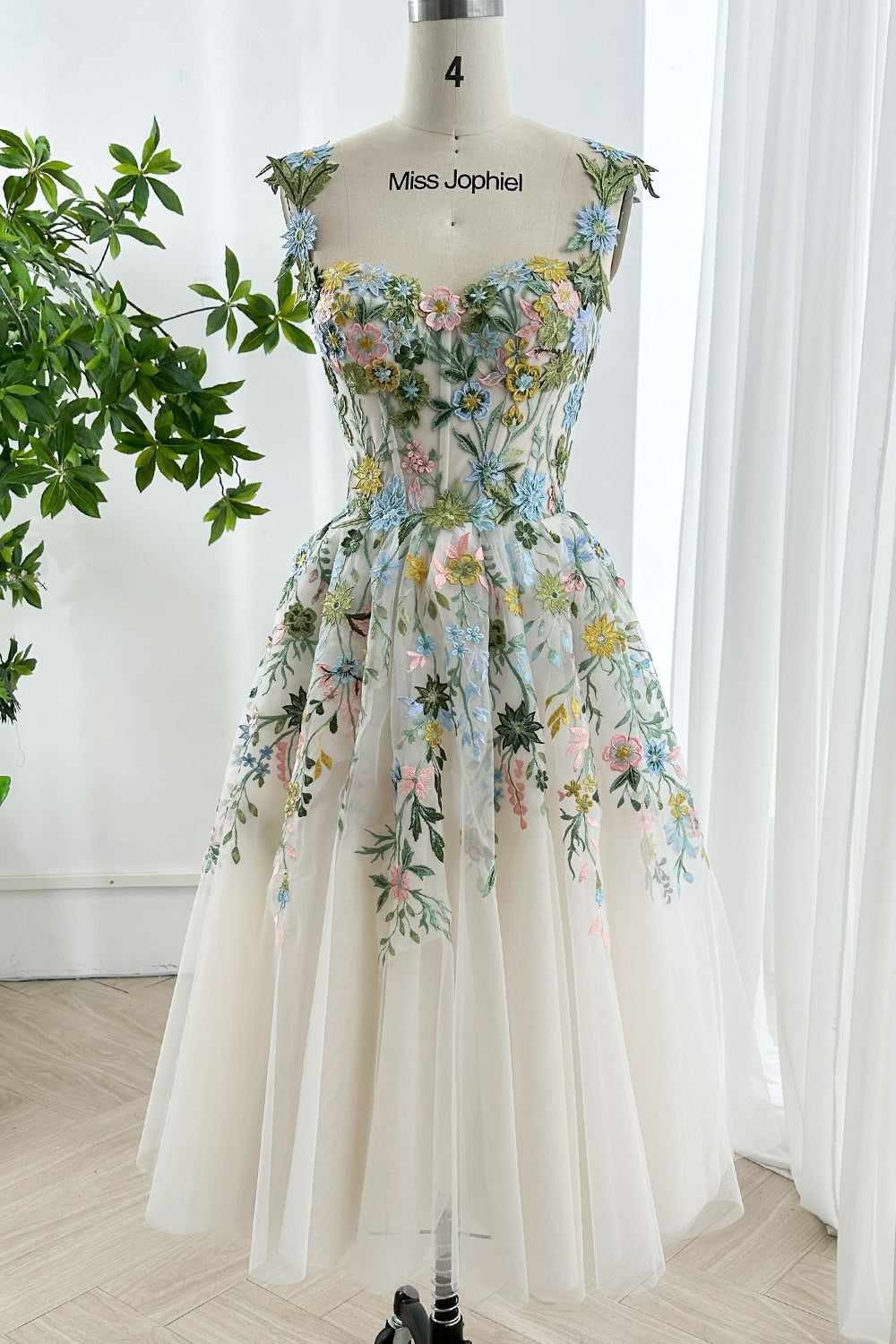 Tea length pastel embroidered lace up back tulle gown on mannequin showcasing intricate floral embroidery in bright daylight studio