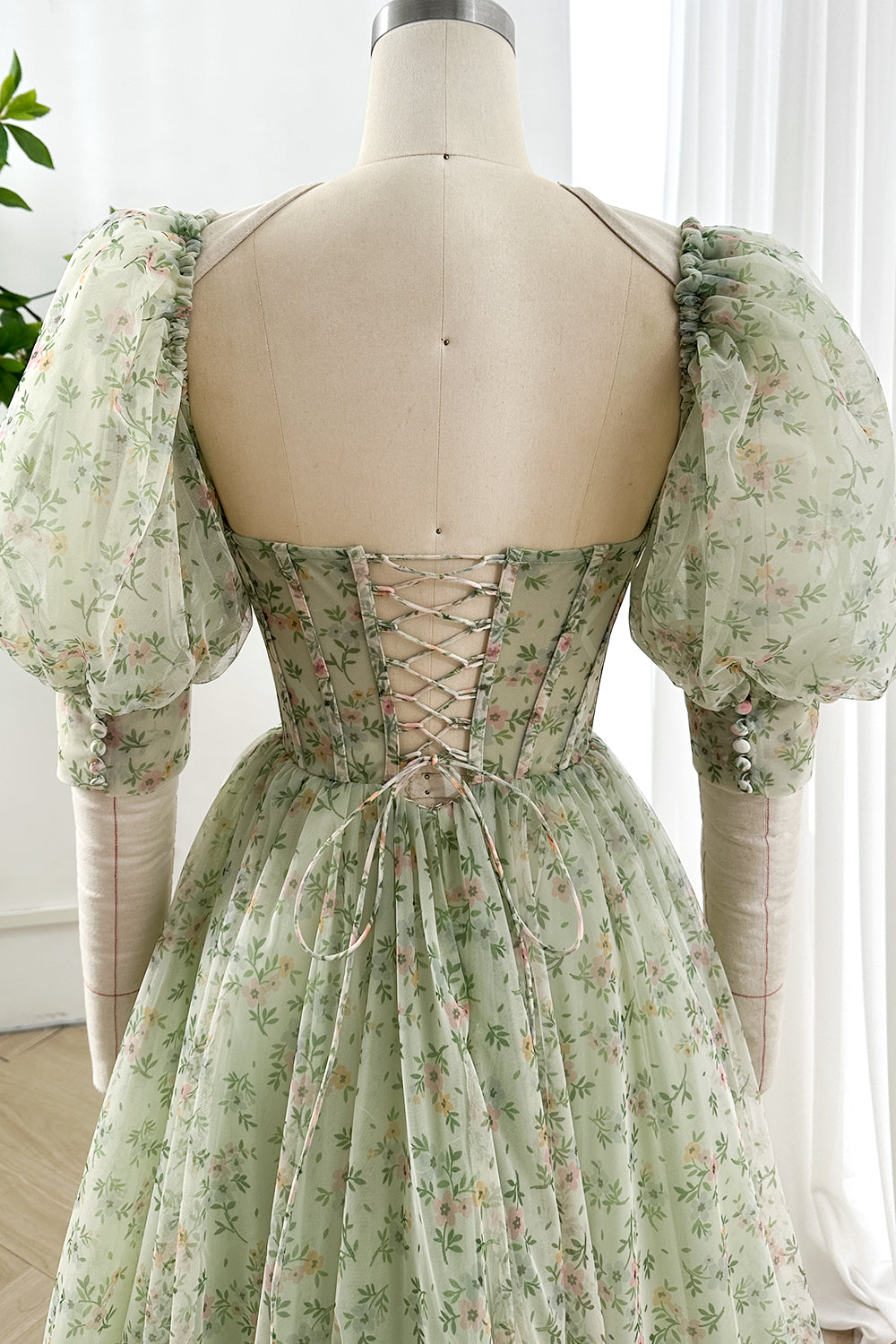 Closeup of chiffon floral gown back showing lace-up corset and puff sleeves crafted in green tulle for timeless vintage elegance