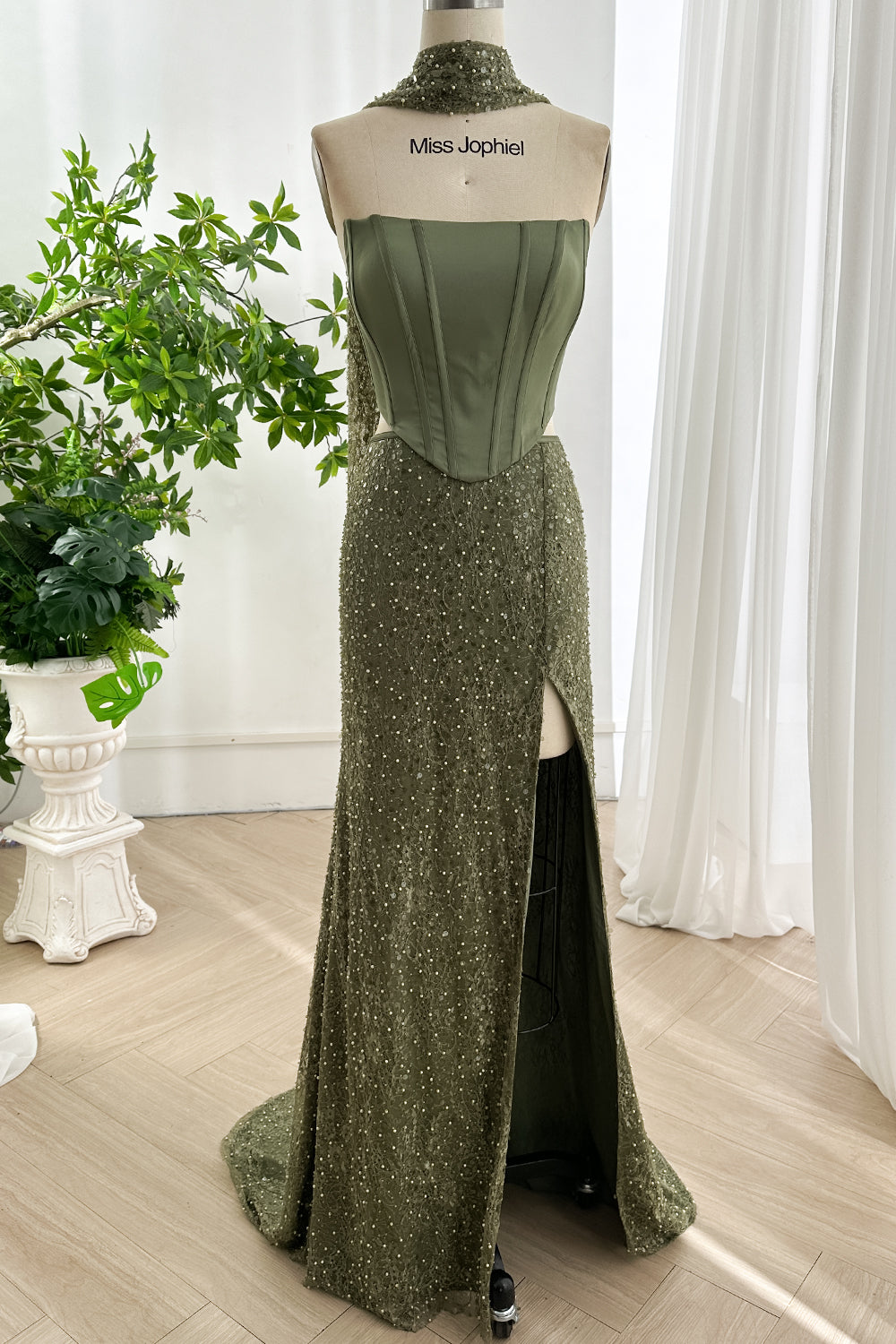 Elegant olive green two piece gown with satin corset top and beaded high slit skirt displayed on mannequin in bright studio