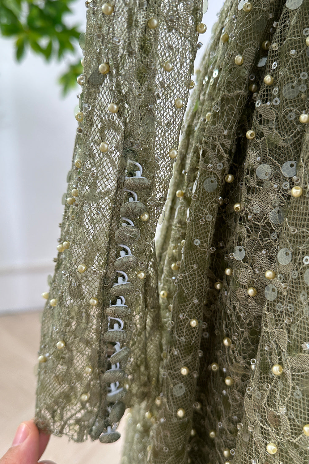 Detailed sleeve cuff with covered buttons and small pearls on olive lace fabric highlighting craftsmanship of beaded long sleeve dress