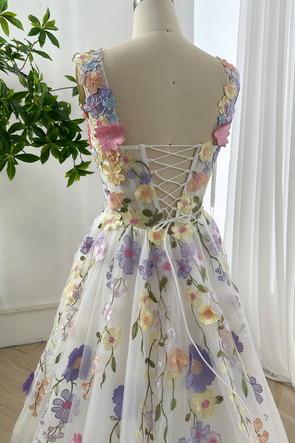 Detailed back close-up of lace-up glitter floral gown showing straps with 3D appliqués and shimmering pastel fabric
