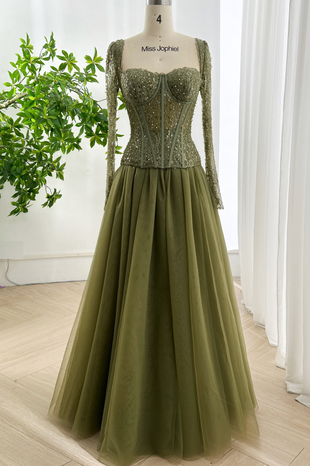 Olive green lace corset gown with full tulle skirt and fitted long sleeves displayed on mannequin in bright studio setting
