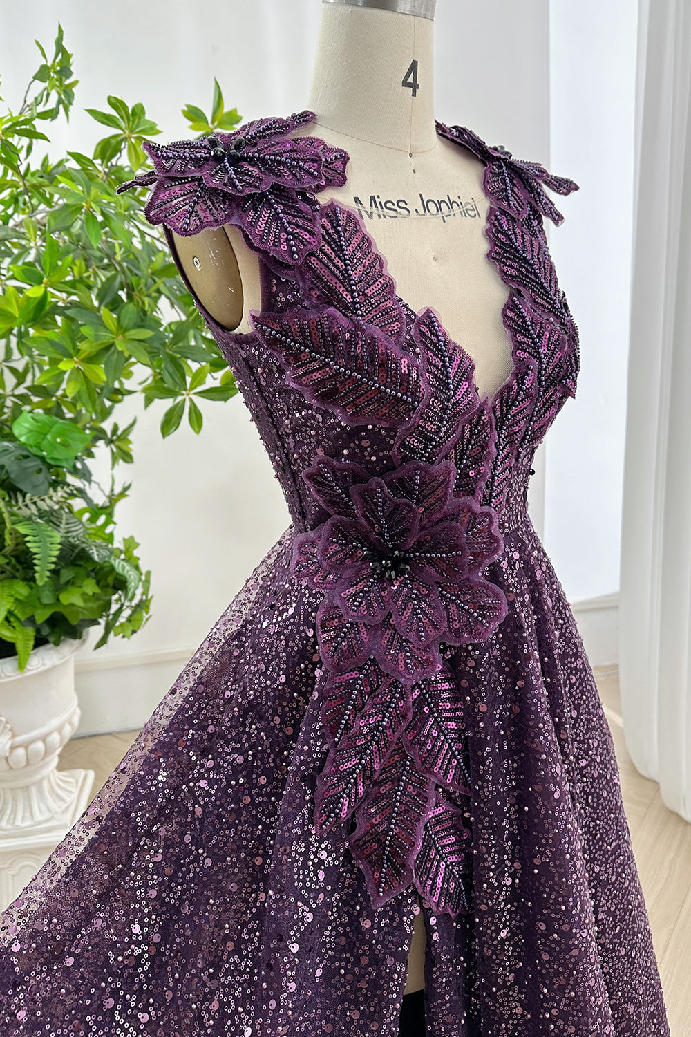 Glamorous plum sequin evening gown with intricate floral and leaf applique on V-neck bodice displayed on mannequin in bright studio