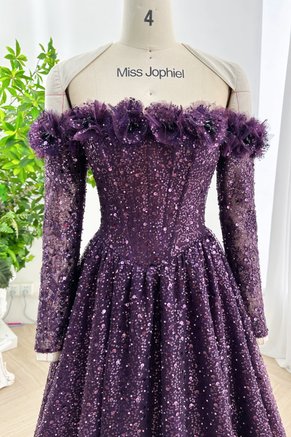 Close-up view of dark purple off-shoulder sequin gown highlighting floral ruffle trim neckline and fitted sleeve design