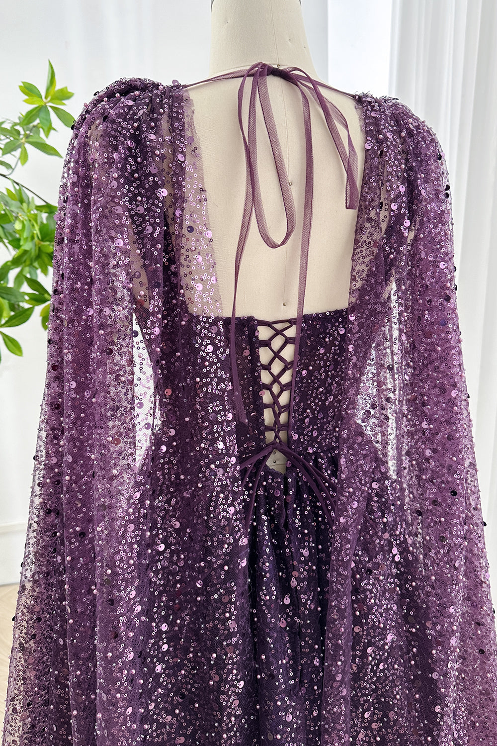 Back view of amethyst sequin lace up corset evening dress highlighting tie straps and elegant flowing cape for glamorous look