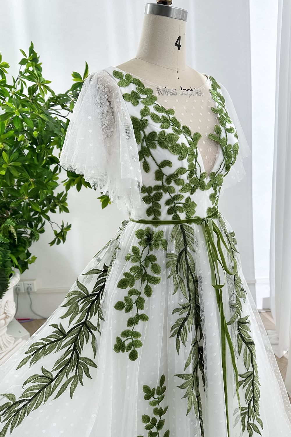 Elegant embroidered green leaf bodice close-up with sheer flutter sleeves and dotted tulle texture