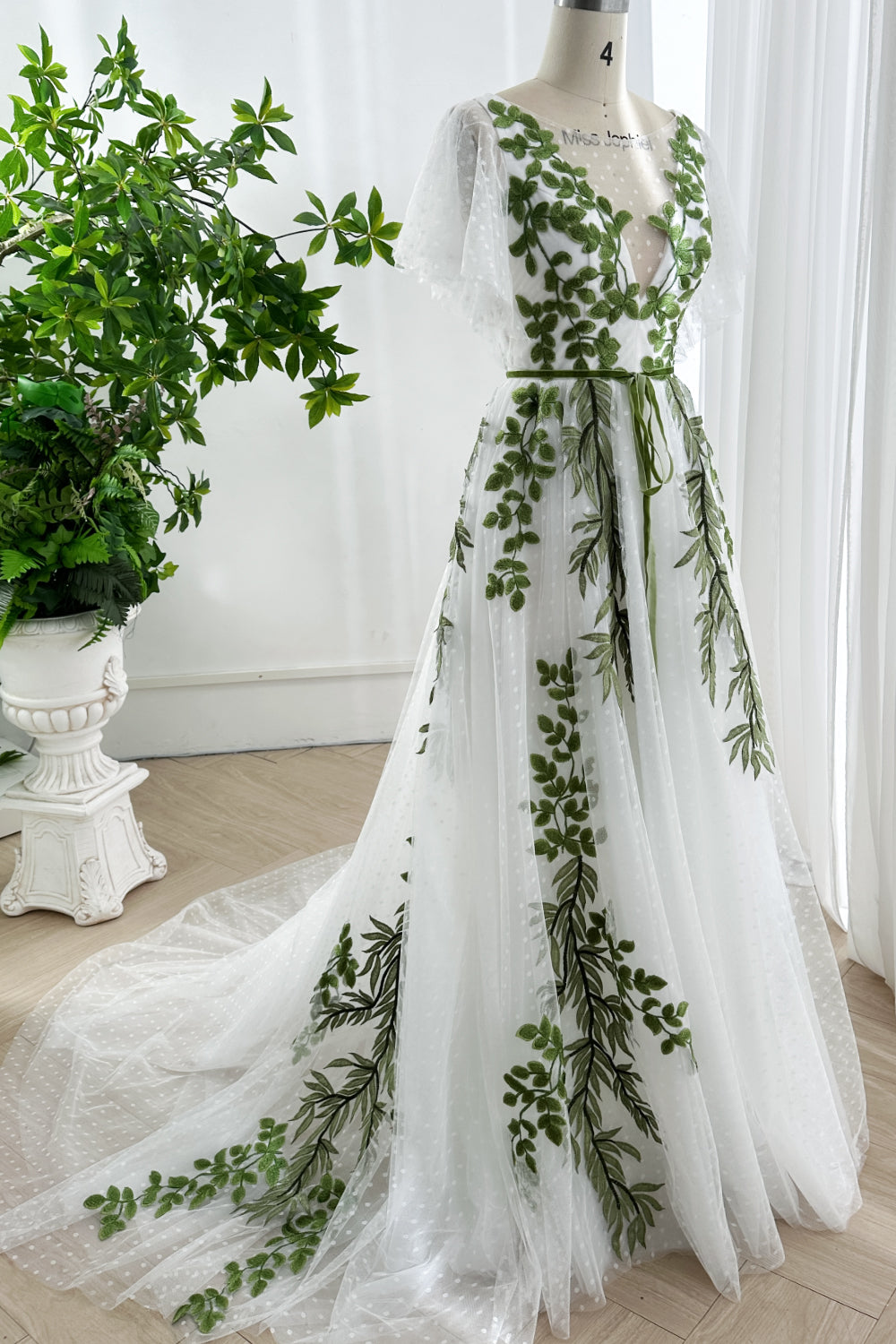 Long embroidered tulle dress with cascading green leaves and full-length skirt displayed on mannequin
