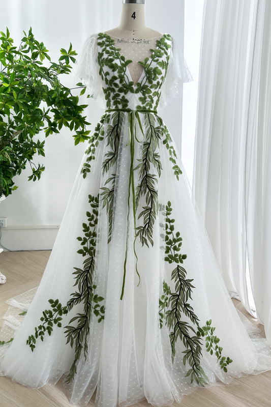 Whimsical white tulle gown with green leaf embroidery and V-neckline on mannequin in natural light setting