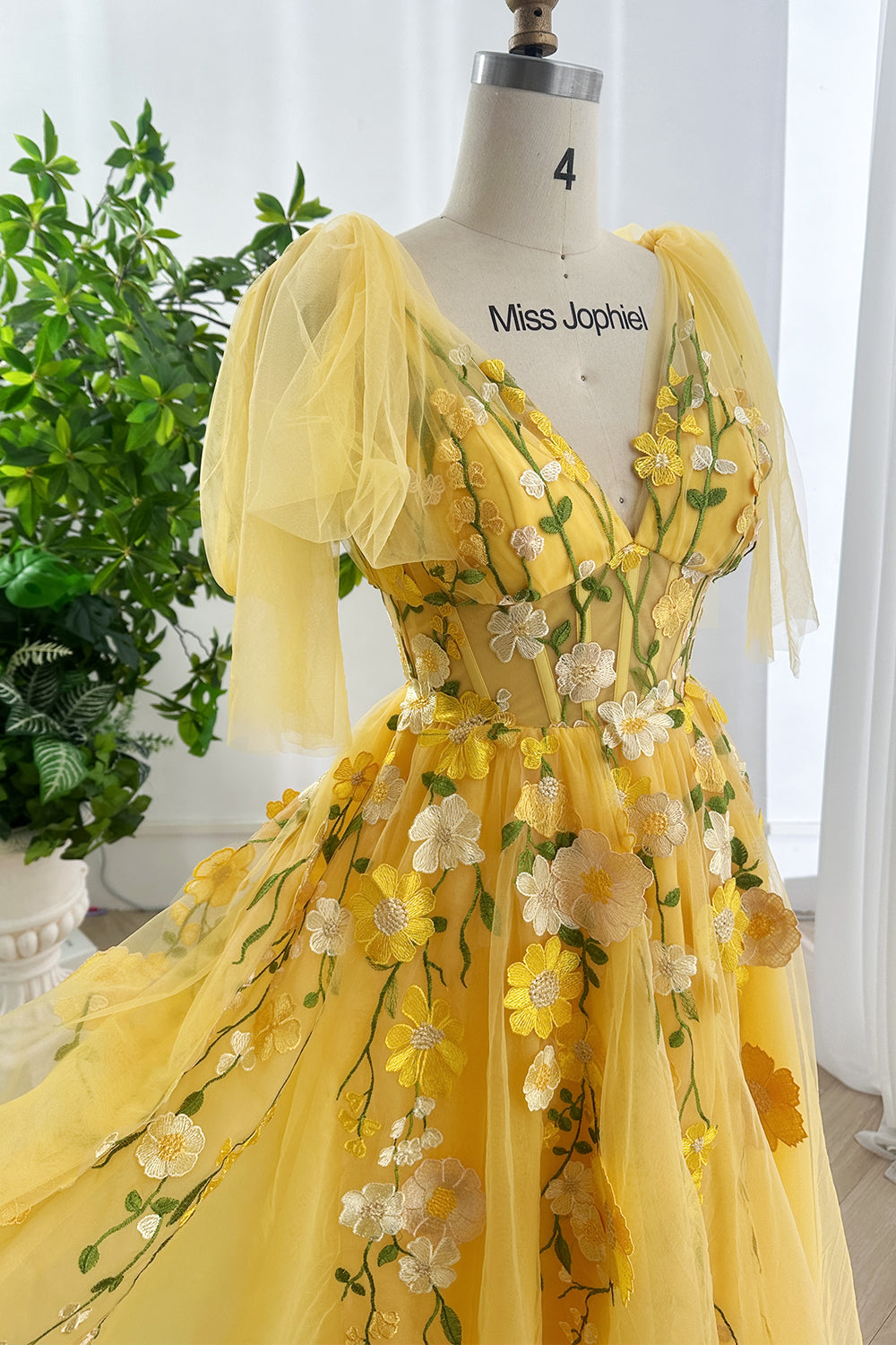 Sunshine blooming embroidered tulle yellow gown featuring whimsical layered floral artistry displayed elegantly on mannequin indoors