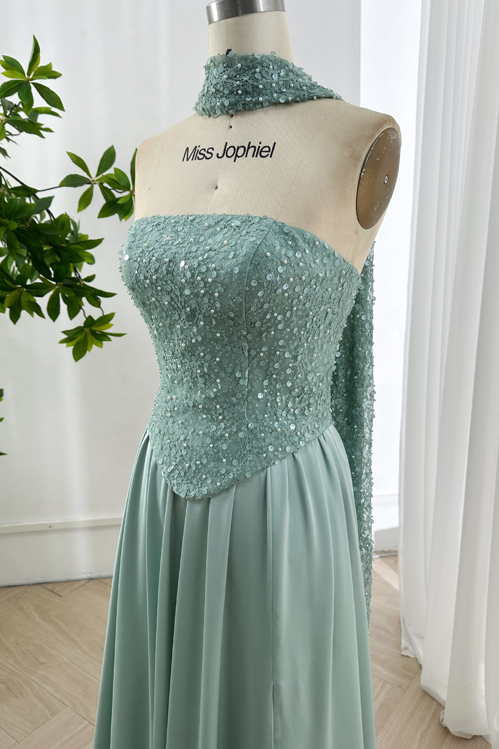 Glistening strapless sage sequin bodice displayed on mannequin highlighting sculpted contour craftsmanship beside foliage backdrop gracefully