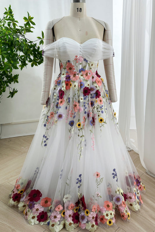 Offshoulder ivory ballgown featuring multicolor embroidered blossoms cascading over tulle skirt displayed elegantly on atelier mannequin