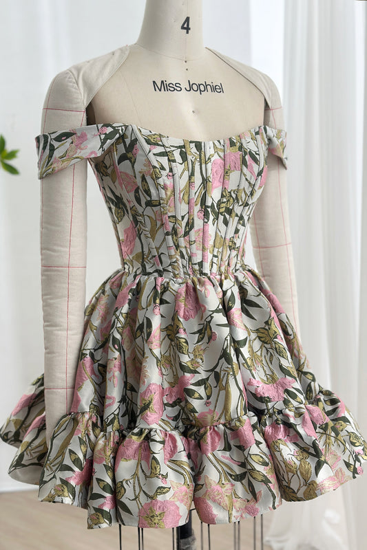 Structured bodice mini featuring blush blossoms sage foliage jacquard texture sculpted waistline ruffled hemline couture presentation mannequin studio