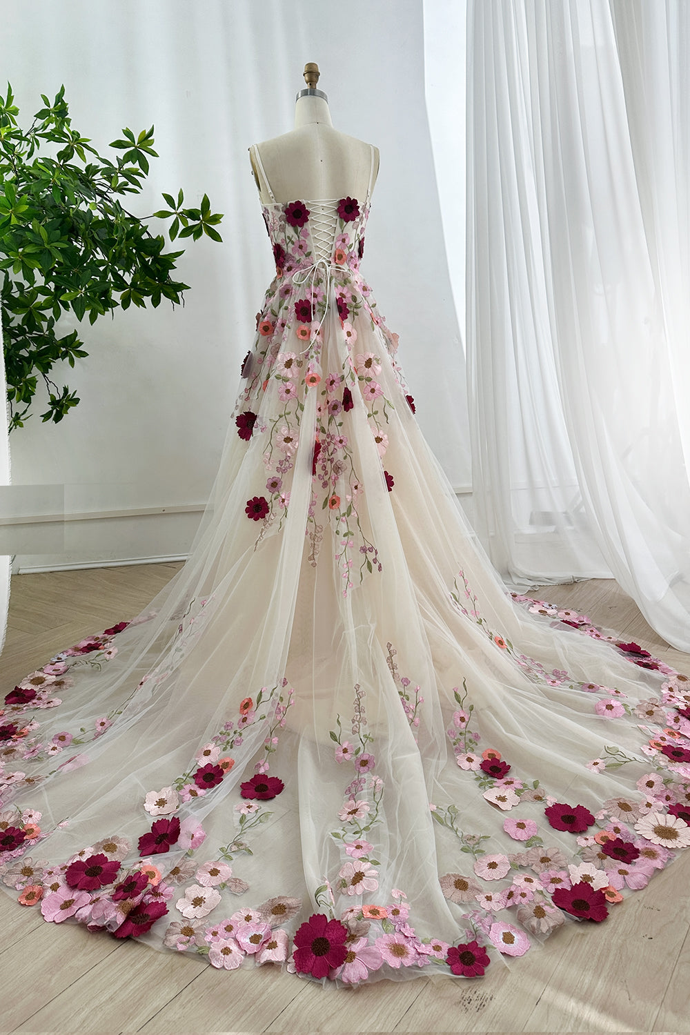 Adjustable laceup corset back showcasing multicolored blossoms flowing dramatically across ethereal champagne mesh silhouette