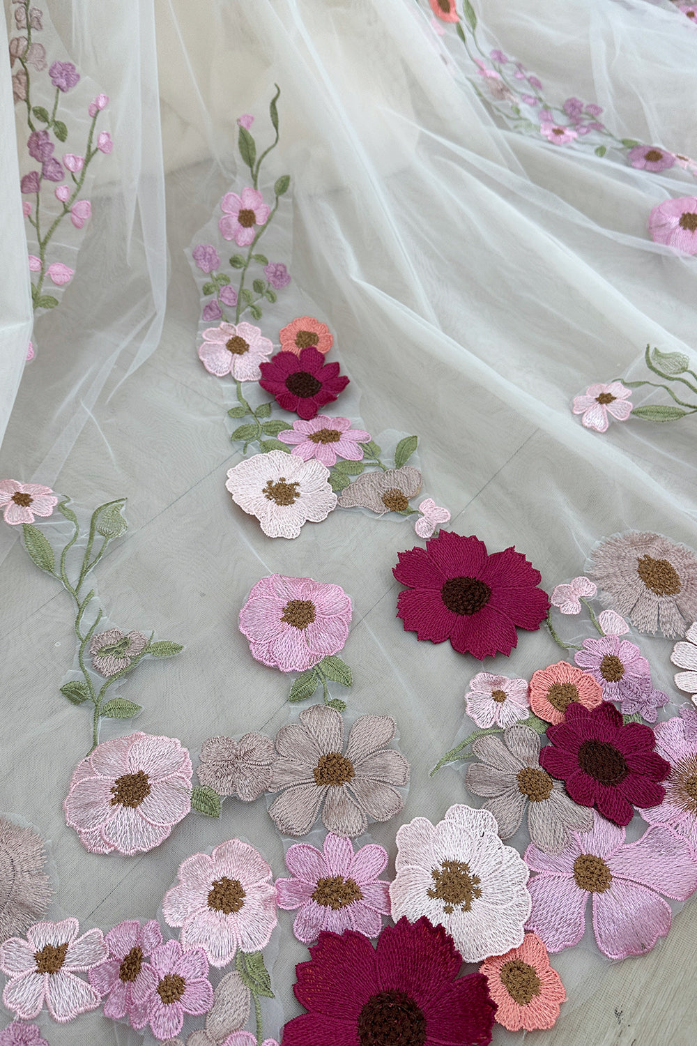 Closeup hemline composition capturing dimensional botanicals arranged artistically over sheer layers against hardwood