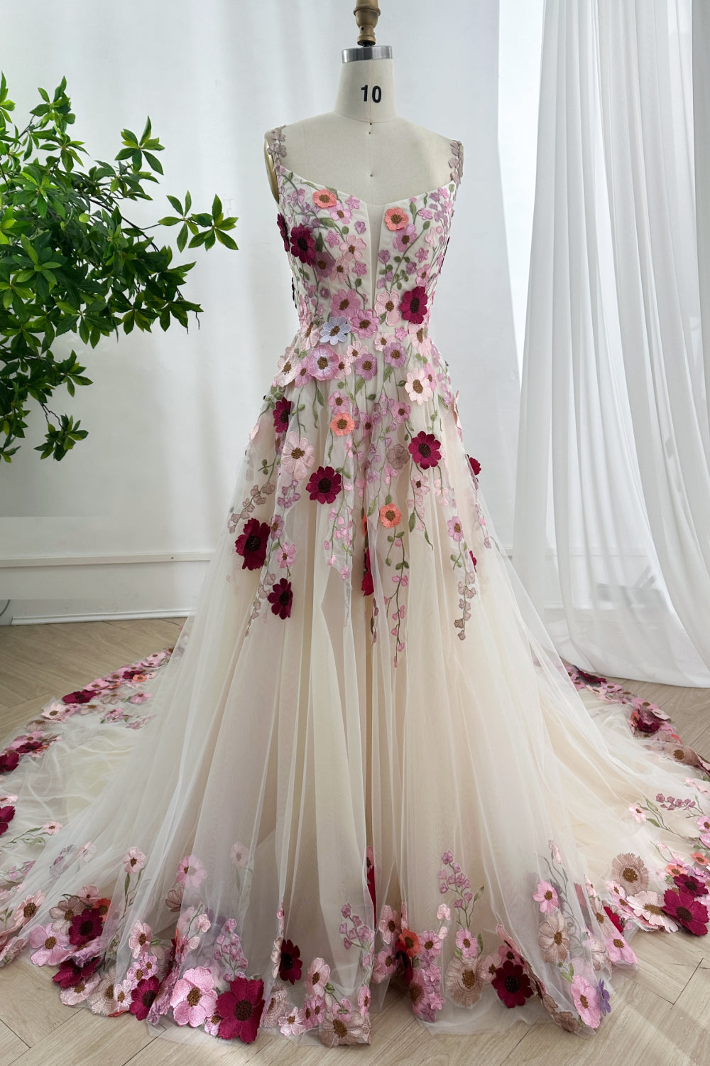 Romantic blush tulle gown featuring cascading botanical appliques sweeping cathedral train displayed upon atelier mannequin