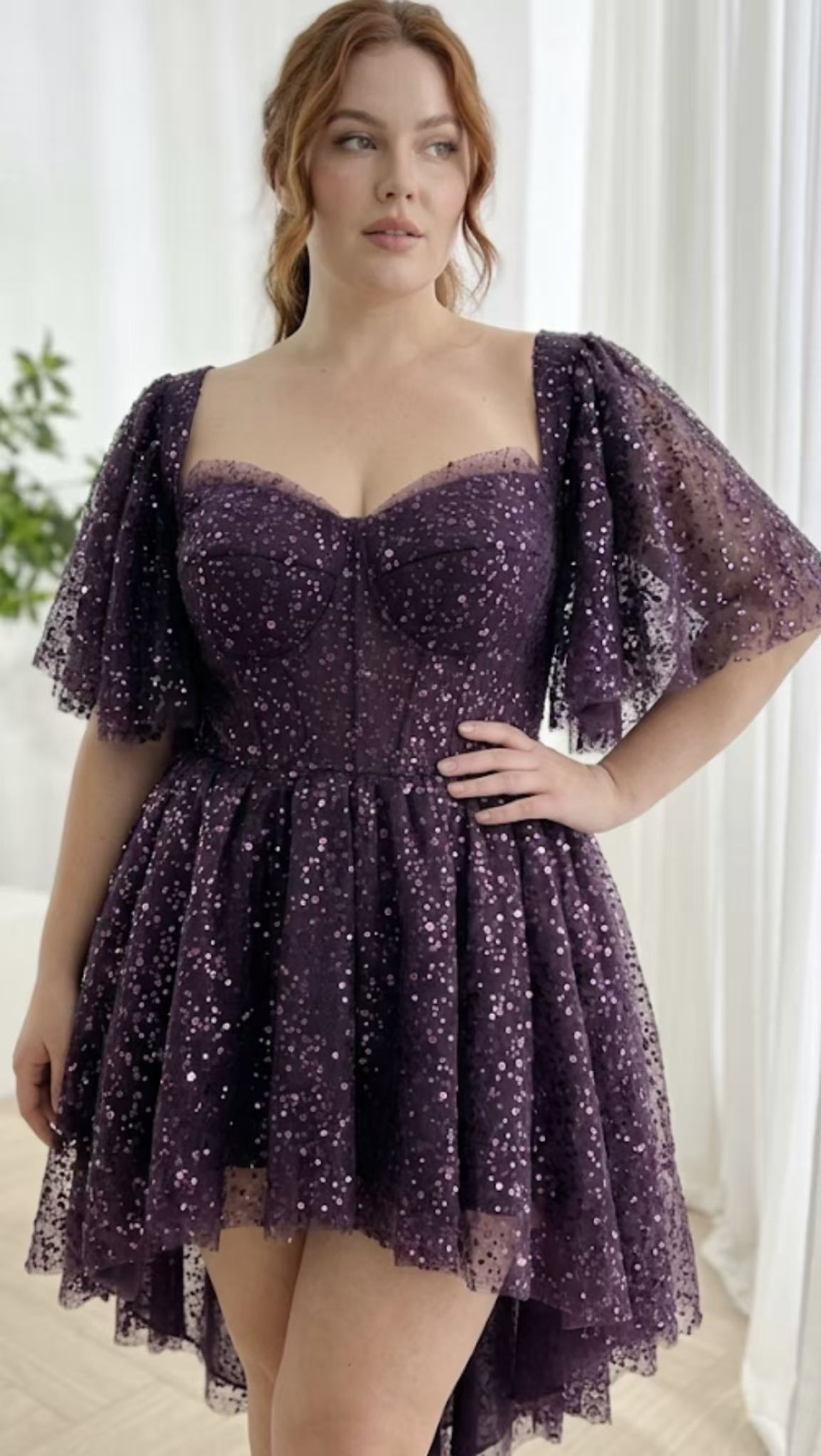 Deep violet sparkle party dress worn model showcasing sweetheart neckline fitted waist sheer sleeves flared hem elegant indoor portrait