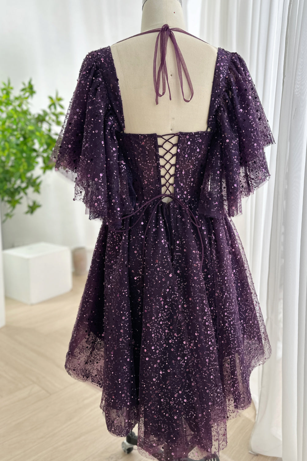 Laceup back sequin tulle evening look revealing adjustable corset closure airy layers flowing silhouette rear perspective bright minimal background