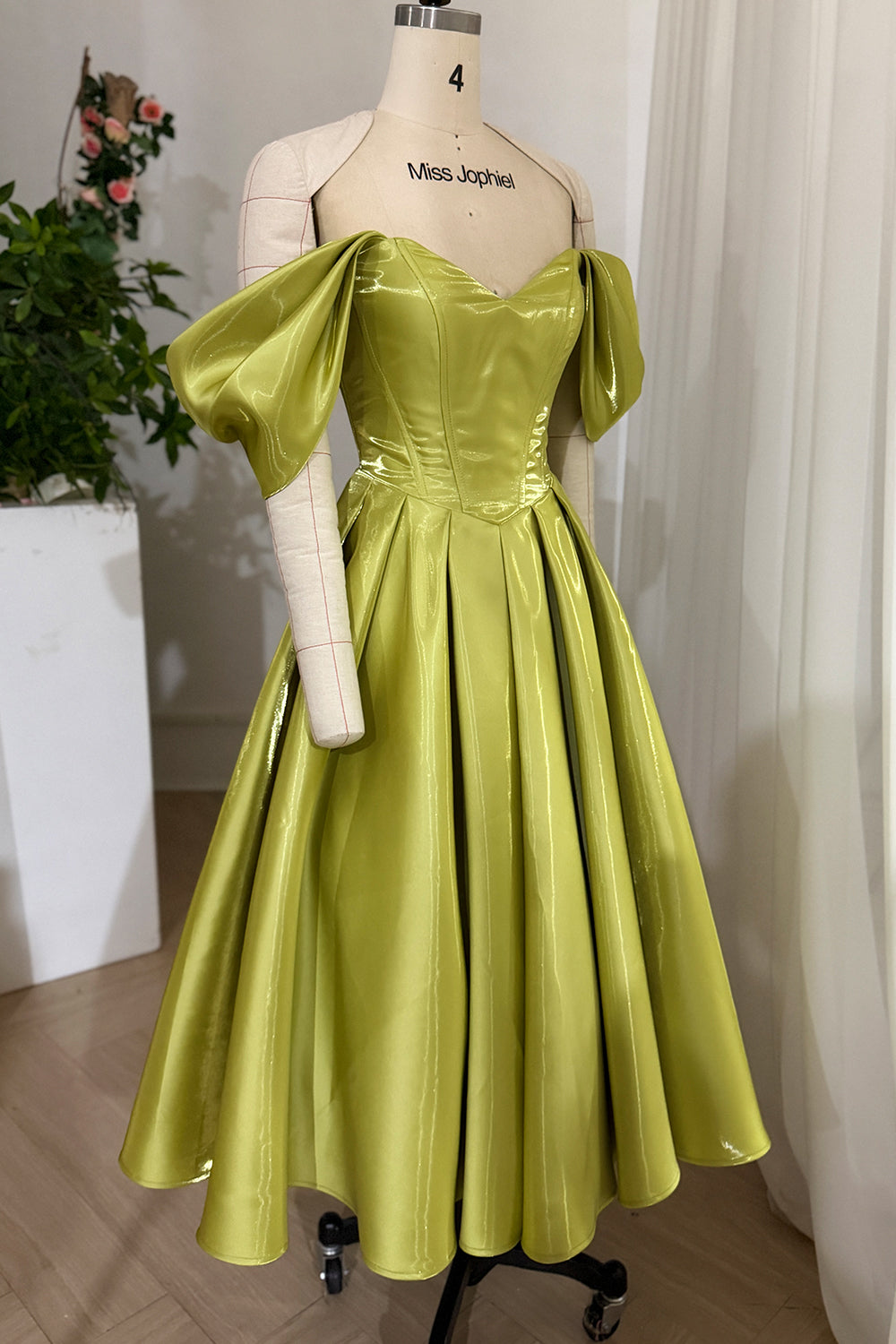 Metallic green princess outfit photographed angled, highlighting voluminous Aline silhouette, corsetry, theatrical sheen