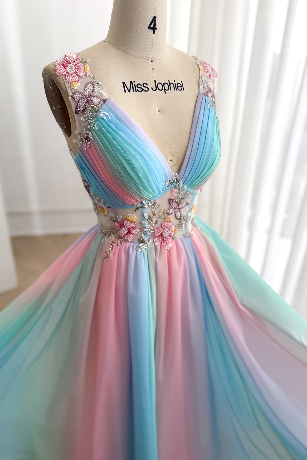 Rear angle shows low V shape, transparent botanical straps, crisscross ties, flowing aqua pink lavender layers graceful sweep