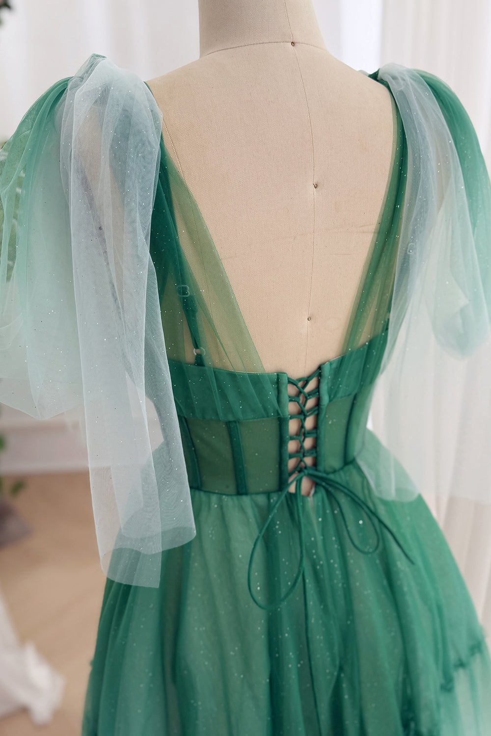 Open-back jade lace-up frock highlighting transparent straps, structured waist, airy bows, couture party details indoors now.