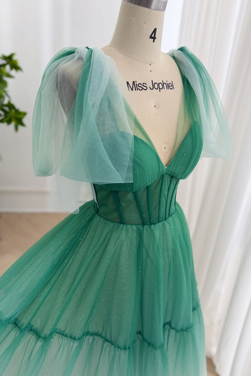 Closeup emerald glitter tulle gown showing V-neck corset bodice, boning, puff shoulder drapes, MissJophiel mannequin studios.