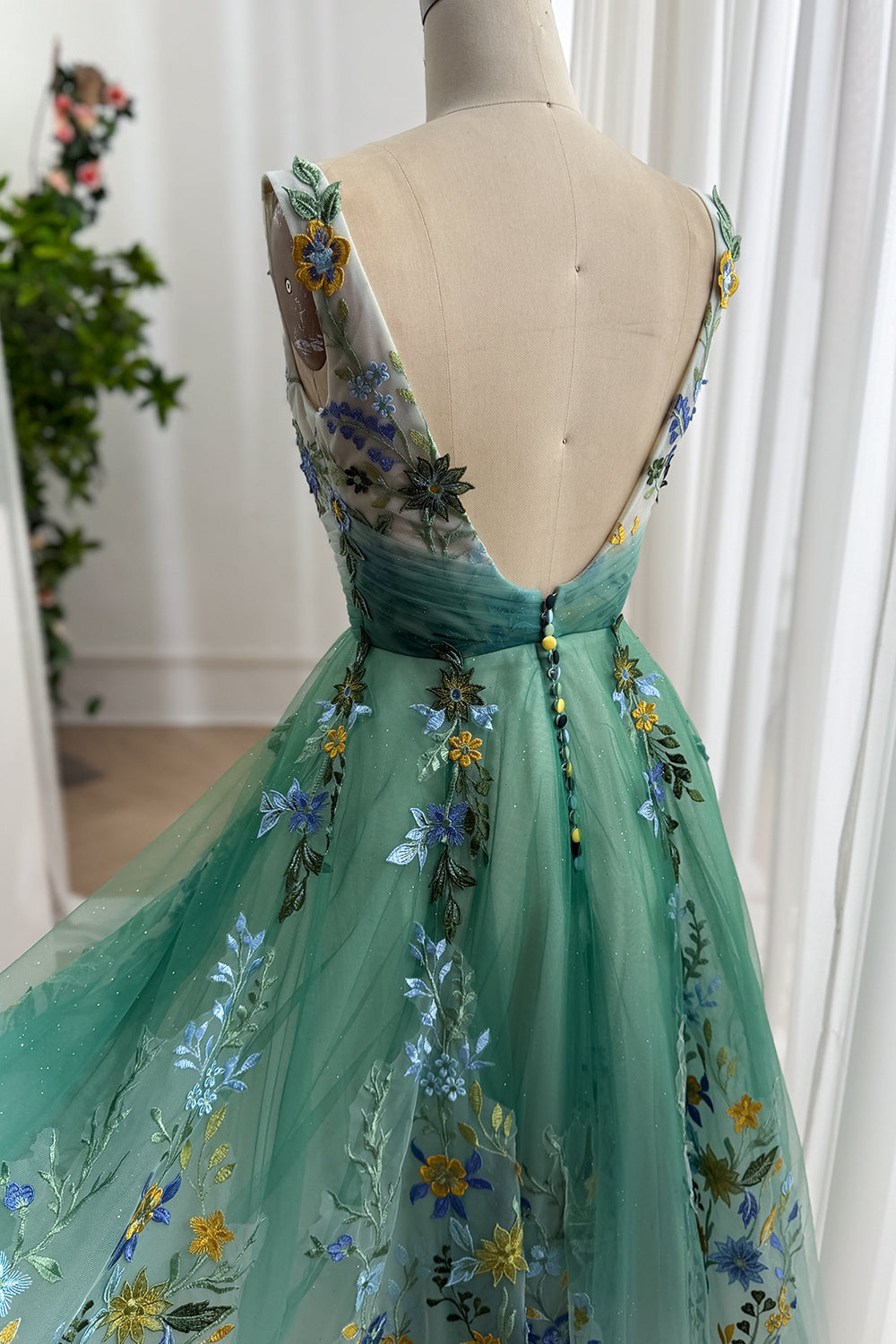Low open back view highlights covered buttons, leafy appliques, airy net layers, elegant garden formalwear styling gracefully