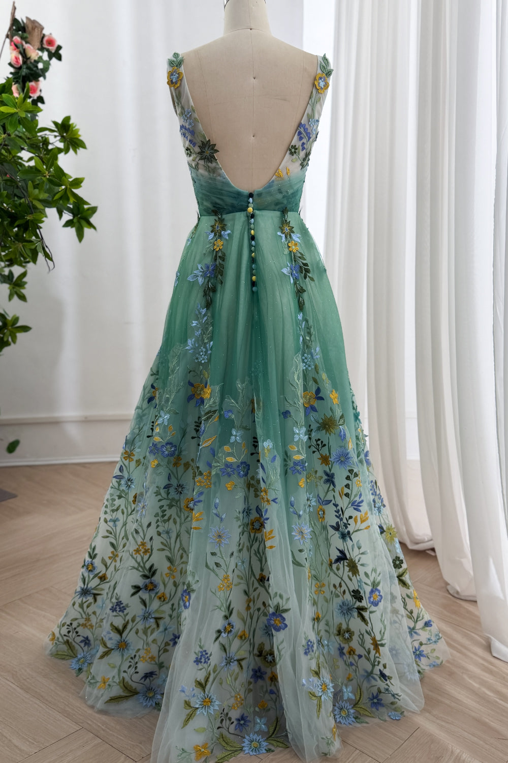 Rear angle captures flowing A-line silhouette, translucent train, couture floral texture, romantic occasion showroom mood set