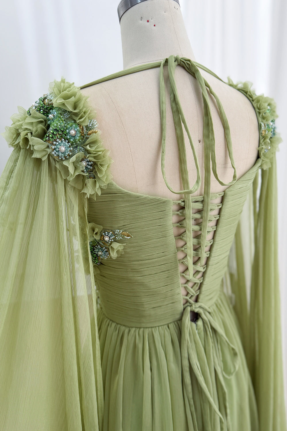 Back view highlights corset lacing, shoulder flower clusters, open neckline, trailing ties, custom garden celebration