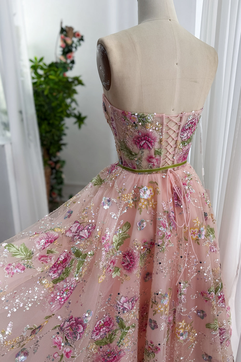 Back view displays lace up closure, sheer overlay, blossom embroidery, flowing volume beside white curtains. calm atelier set